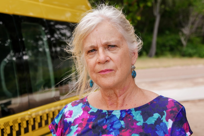 A woman stands serious in front of a yellow taxi on Magnetic Island.