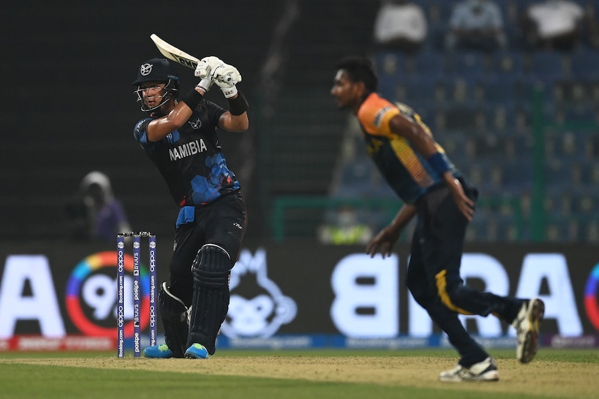 A batsman drives the ball through the covers as the bowler watches on during a T20 match. 