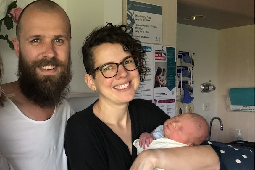 A man and a woman are both smiling and the woman is holding a newborn baby