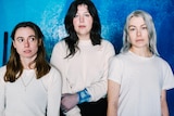 Julien Baker, Lucy Dacus and Phoebe Bridgers stand in white tops with serious expressions looking at the camera,