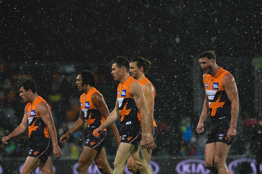 Five Giants players walk in the same direction. Snow falls on them.