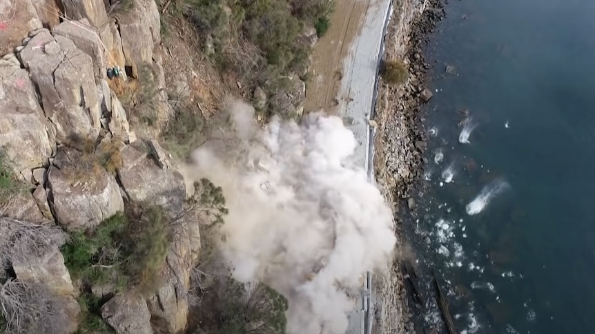 Rocks fall on a road in a controlled explosion.