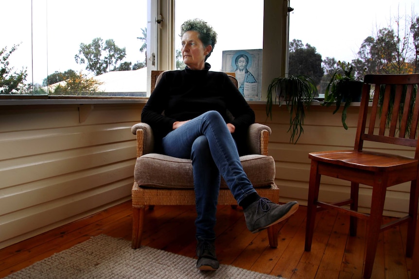 Kate Engelbrecht sits in her home in Mudgee, with Catholic iconography behind her.