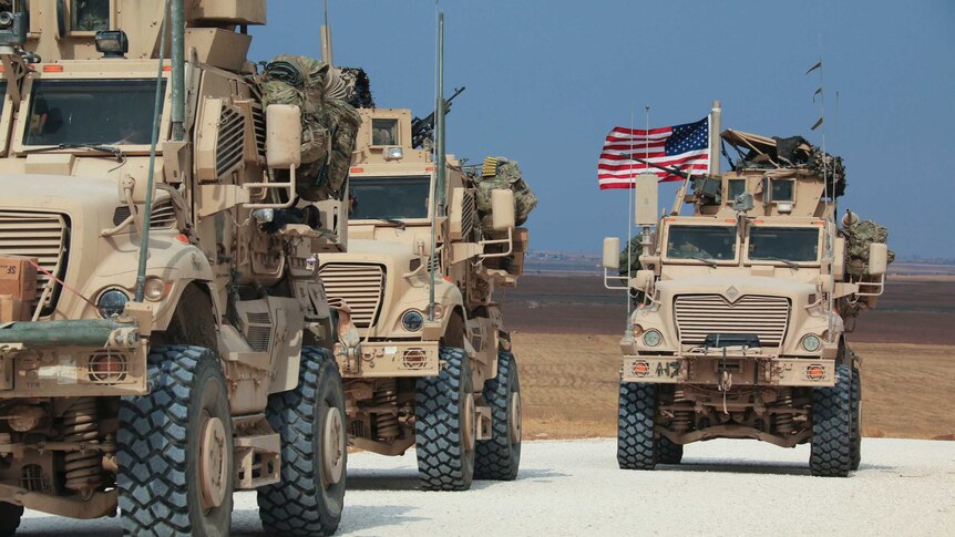 American military convoy of trucks with US flags flying stop along a dirt road.