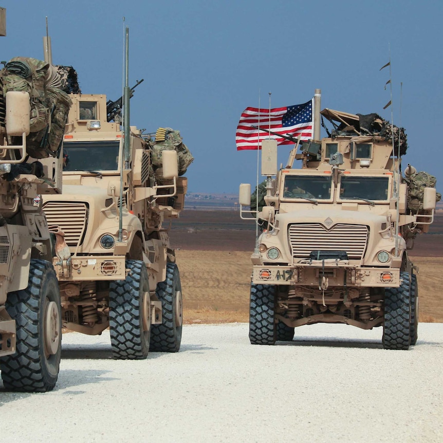 American military convoy of trucks with US flags flying stop along a dirt road.