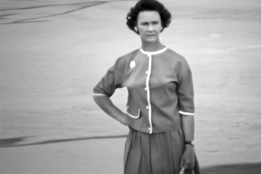 Photo of a stylish woman on a street corner holding a handbag with a messaging device in it.