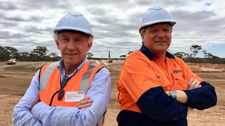 Two men in hard hats stand back to back on mine site
