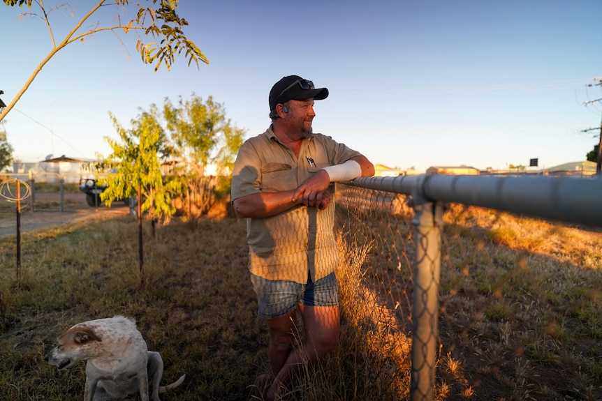 Man wearing brown shirt and black cap standing at fence at sunset