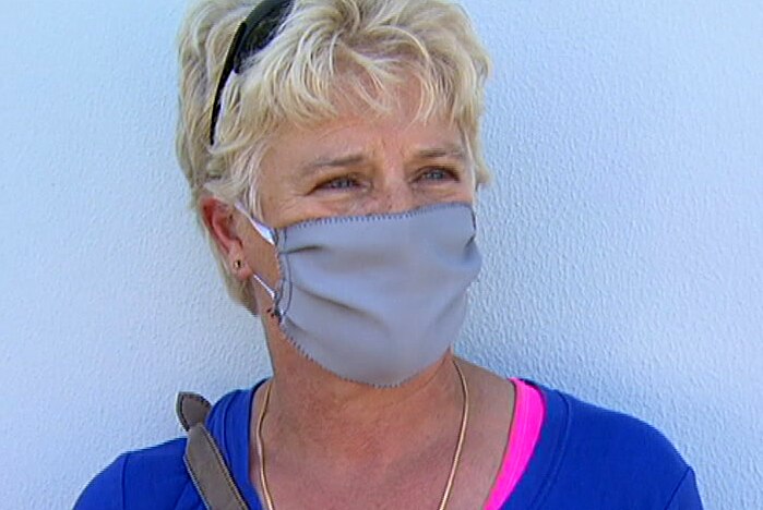 A headshot of a woman in a blue t-shirt wearing a grey face mask.