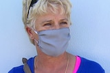 A headshot of a woman in a blue t-shirt wearing a grey face mask.
