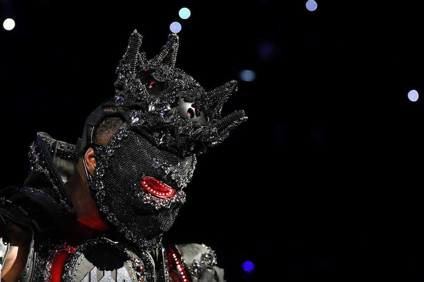 Deontay Wilder wears a large, black, spiked helmet which is covered in sequins and lights.