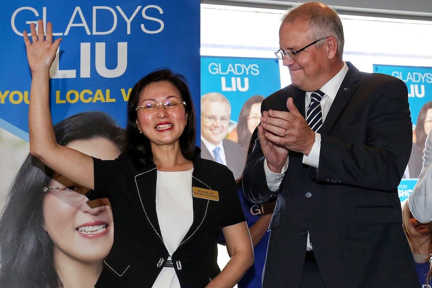 Scott Morrison, wearing suit, applauds Gladys Liu, who is waving in front of posters bearing her face and name.
