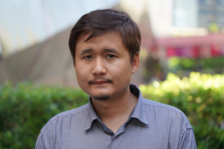 A man wearing a collared shirt looks at the camera with a polite expression on his face