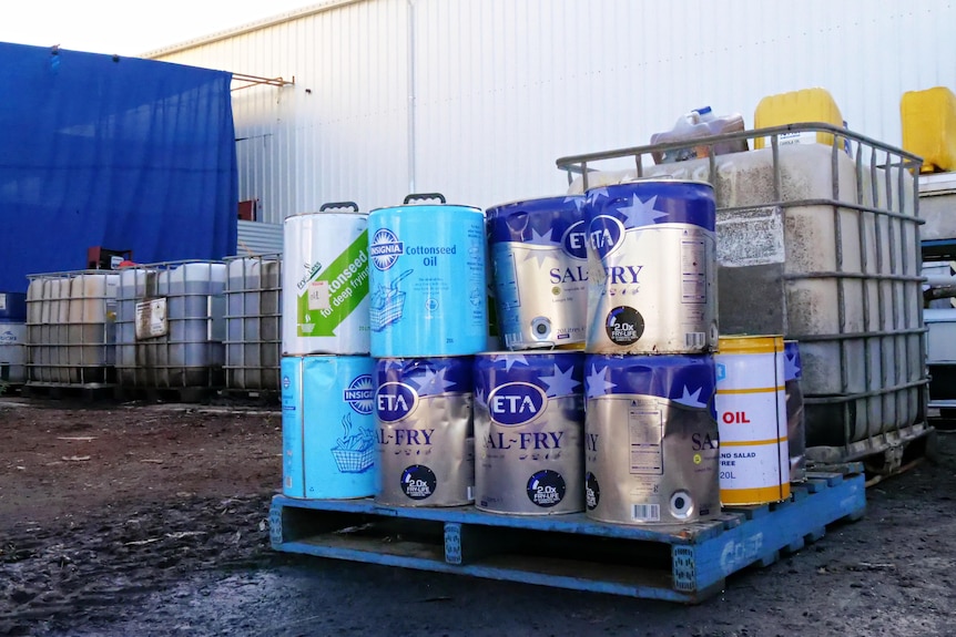 Cans of oil on a pellet in the foreground, plastic tanks containing oil in the background.