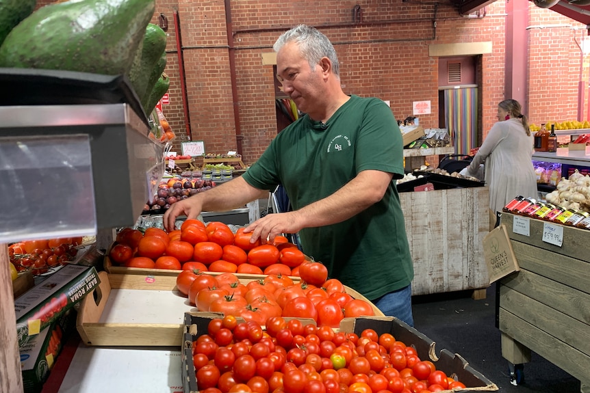 A male shop owner in a green shirt organises a fruit shelf.