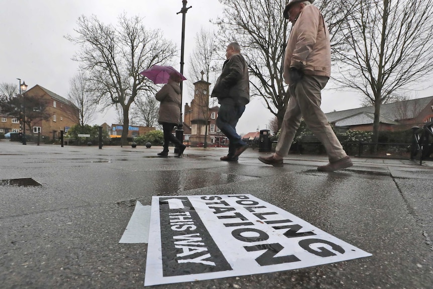 People walk in the rain to a polling booth during the UK general election