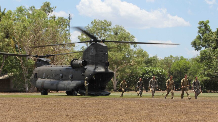 Military personnel with hunting spears disembark from a Chinook helicopter in the Australian outback.