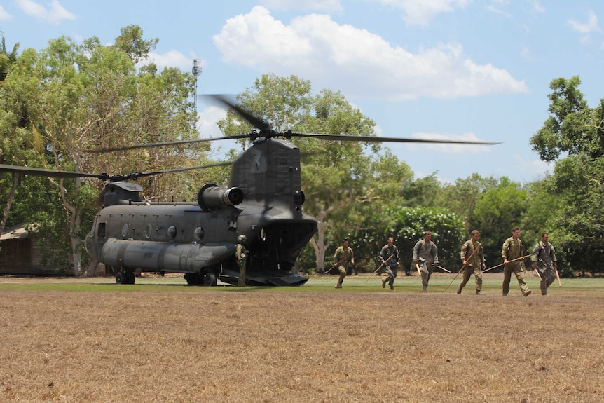 Military personnel with hunting spears disembark from a Chinook helicopter in the Australian outback.