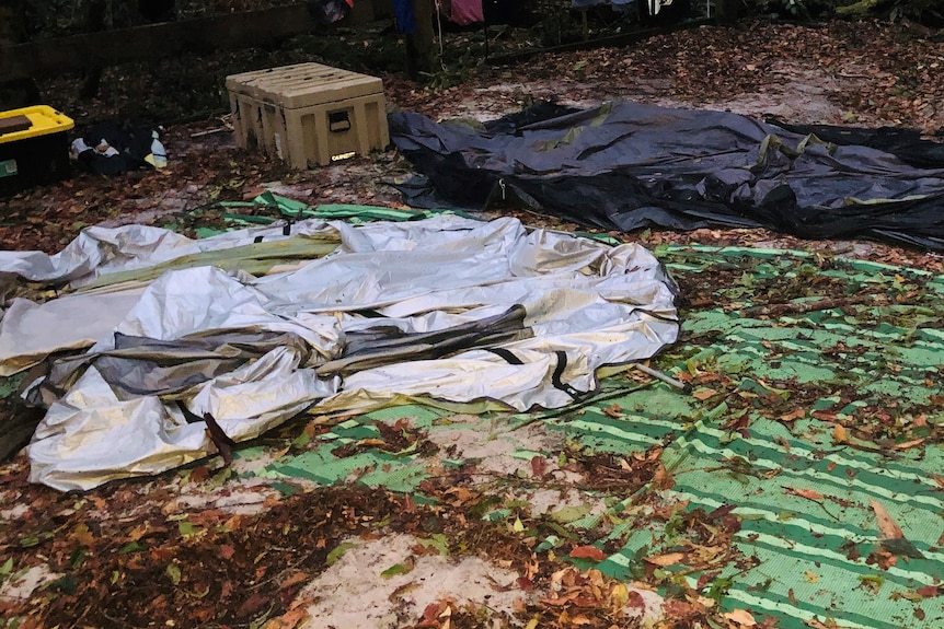 A flattened tent with poles on the ground and dirt and leaves over the remains of the tent.