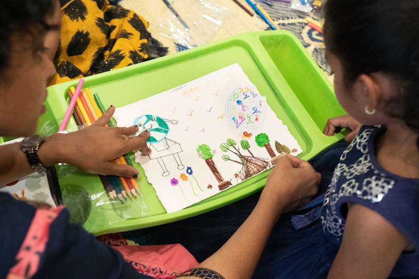 A young girl and her mother look at a child's drawing of nature. 