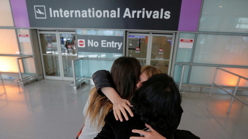 Relatives hug in front of the international arrivals sign at an airport