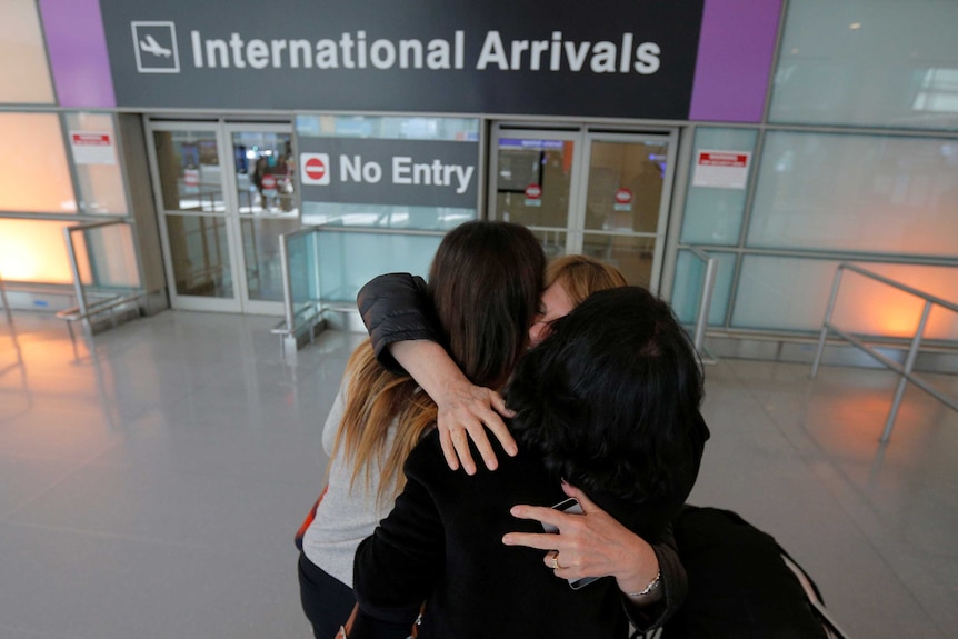 Relatives hug in front of the international arrivals sign at an airport