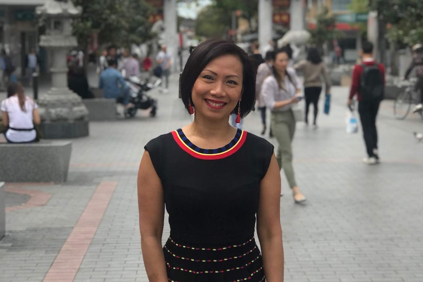 Asian lady standing in street with asian arches in background.