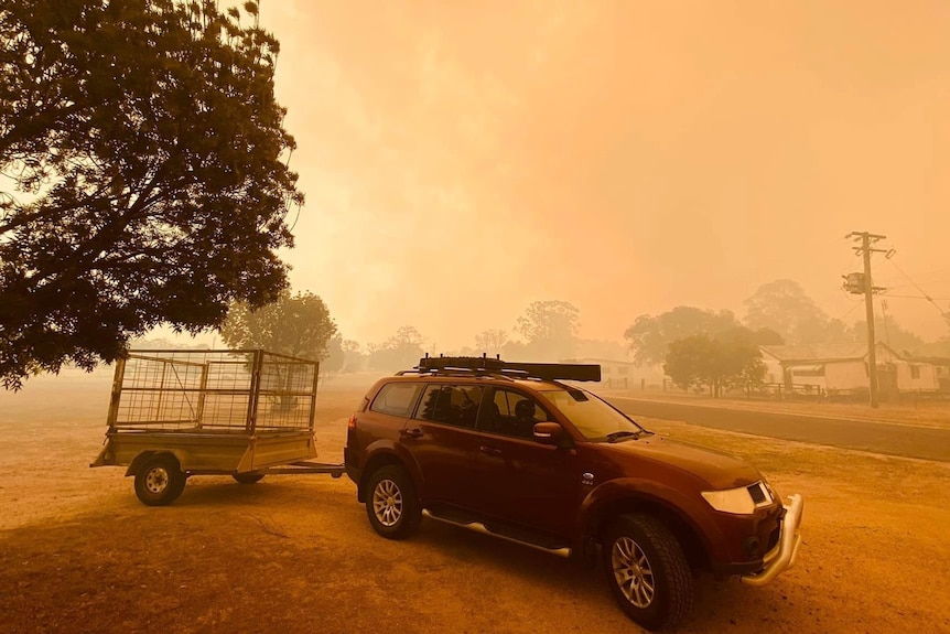 A car and trailer parked near a road, with bushfire smoke making the whole scene look orange