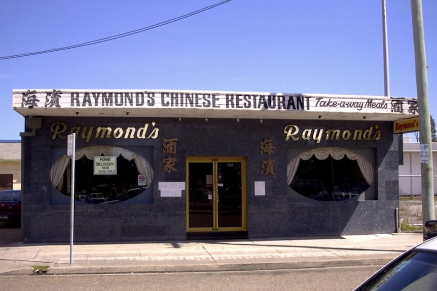 The front of a blue, single storey restaurant called Raymond's Chinese takeaway, which has two large windows and a central door.