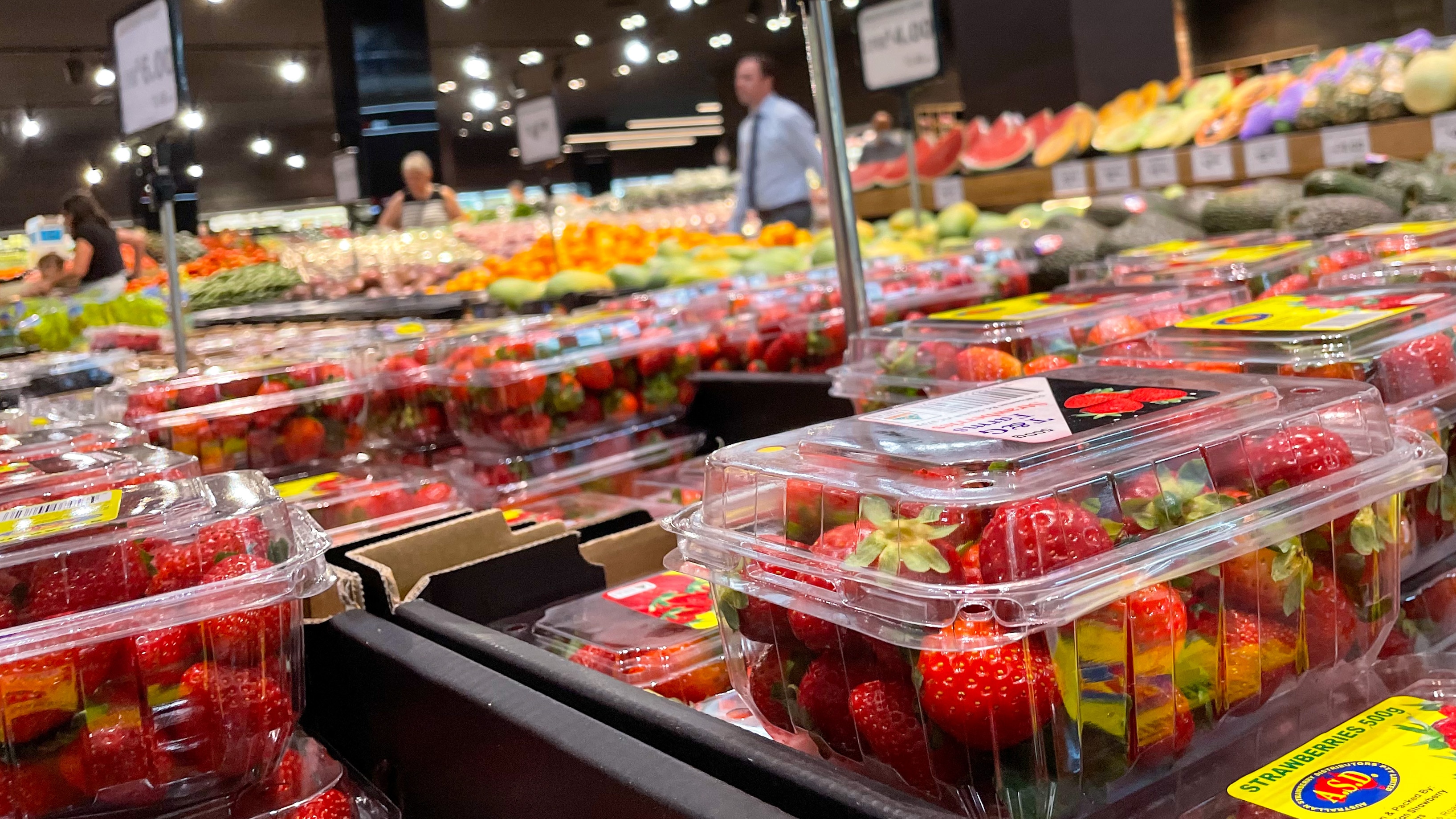Punnets of strawberries on display, with people walking through the supermarket in the background 