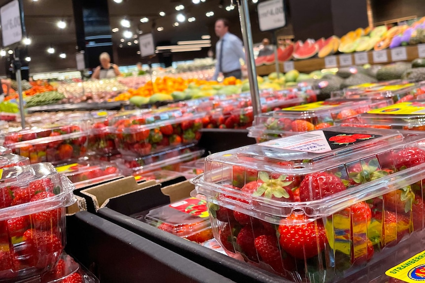 Punnets of strawberries on display, with people walking through the supermarket in the background 