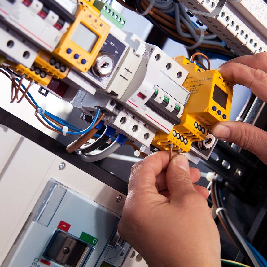 Hands work on electrical equipment.