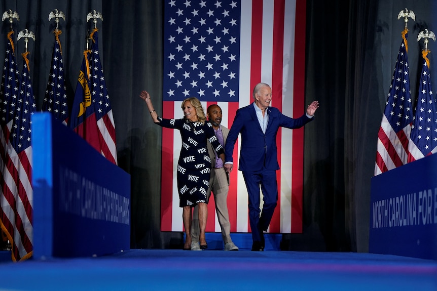 Joe and Jill Biden wave as they enter a stage draped with US flags.