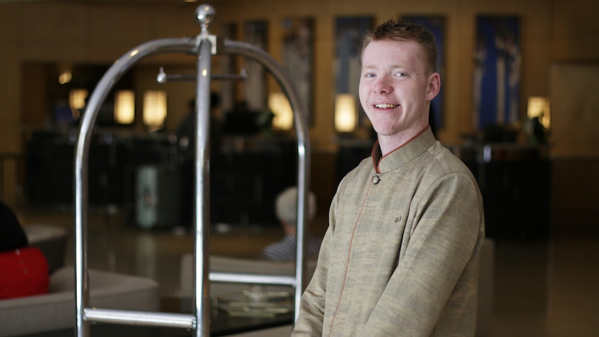 A young white man with short hair working as a bell boy in a hotel lobby 