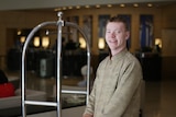 A young white man with short hair working as a bell boy in a hotel lobby 