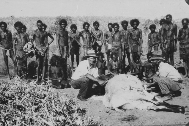 Black and white photo from ca 1930 of Aboriginal men in chains and Aboriginal women sitting in front of them