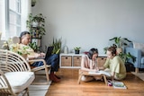 A man sitting on a chair using a laptop while two women sit on the floor writing in books