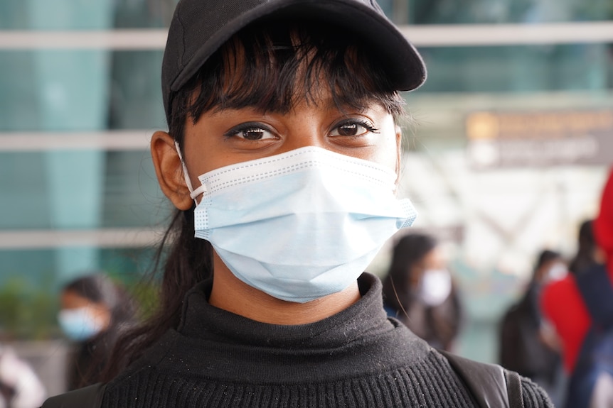 A young Indian woman in a black baseball cap and a blue medical face mask