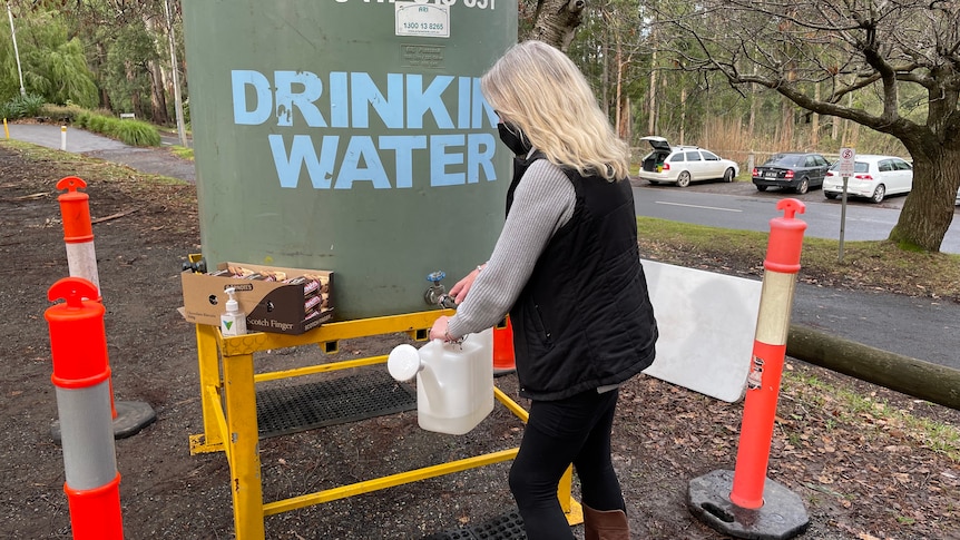 A woman fills a container with water from a large tank outside. 