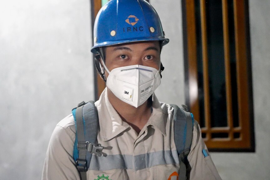 A worker wearing a hat and mask looks at the camera.