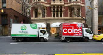 Coles and Woolworths delivery trucks parked side by side on the street.