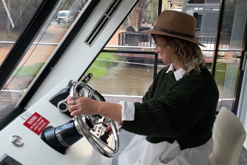 A woman sitting in a houseboat with her hands on a steering wheel