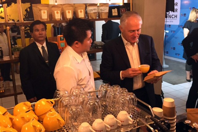 Malcolm Turnbull looks at a up of coffee as he stands next to a cafe owner