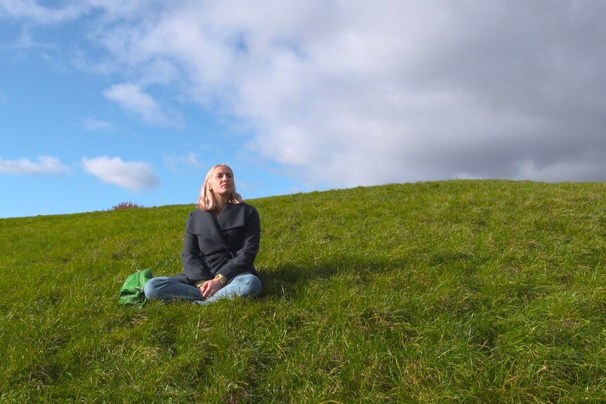 A woman sitting on a grassy hill.