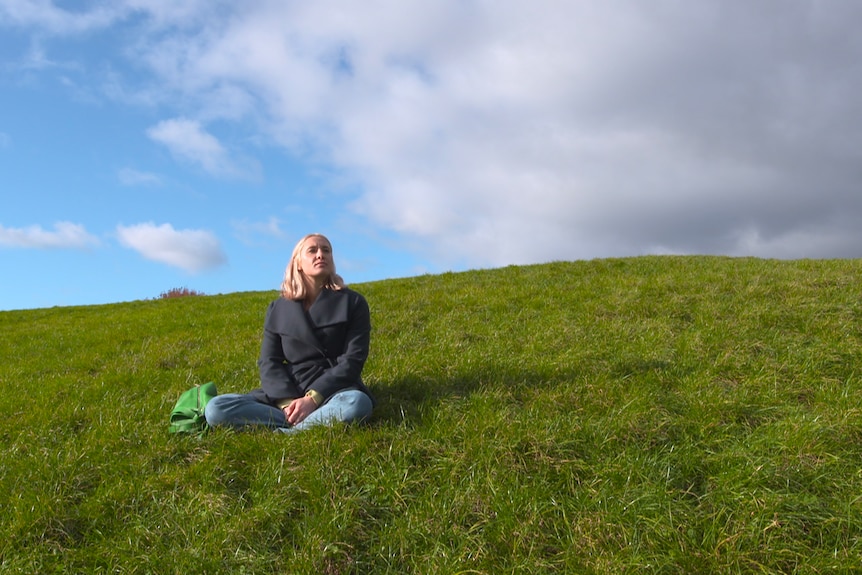 A woman sitting on a grassy hill.