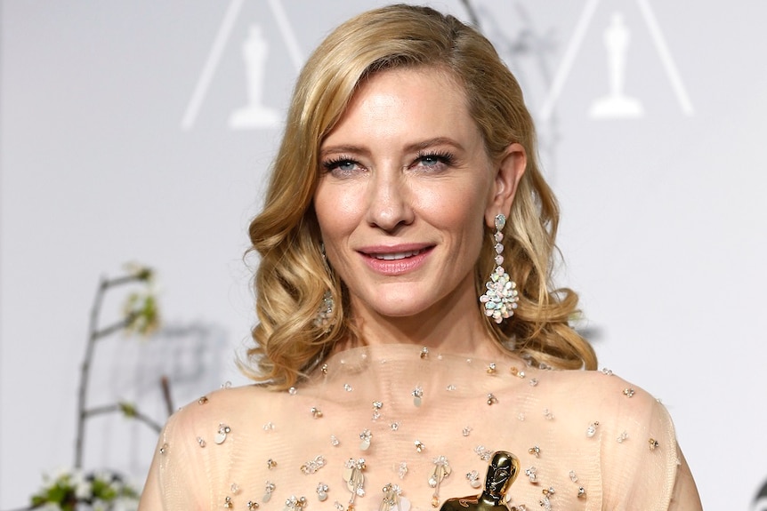 Cate Blanchett holds an Oscar statue, wearing a cream-coloured gown, opal earrings, a diamond bracelet and ring.