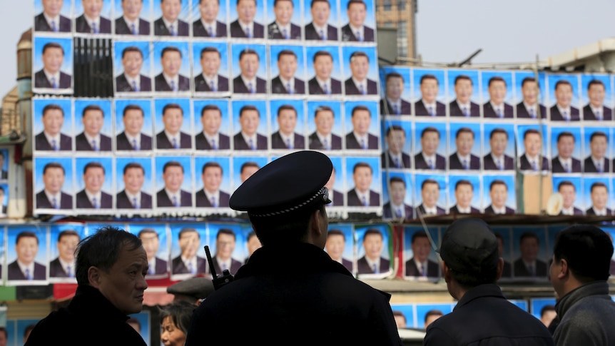 Person in police hat from back with blurry posters of Xi Jinping covering a wall in the background.
