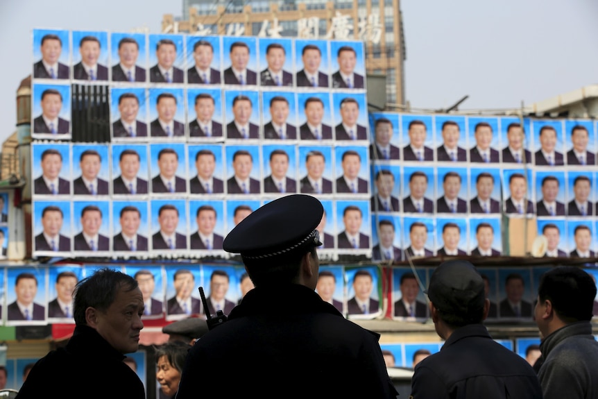 Person in police hat from back with blurry posters of Xi Jinping covering a wall in the background.