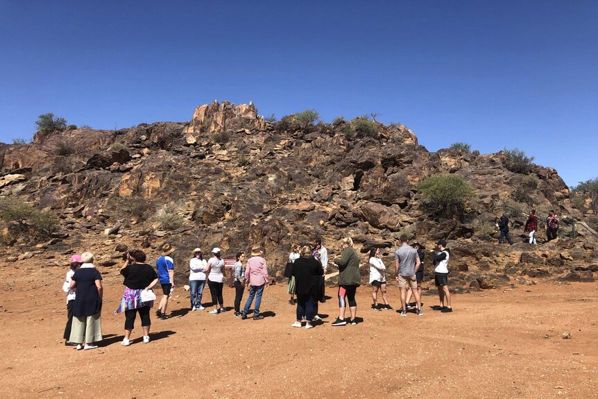 A group of people gathered at the bottom of a rocky, desert hill.