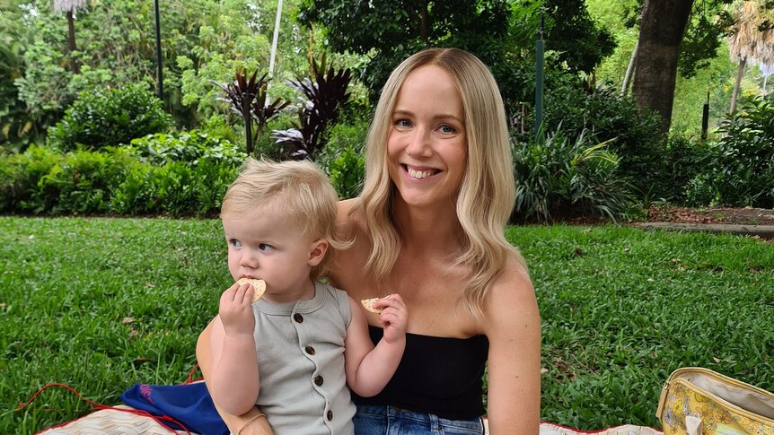 Woman with blonde hair sits in the park with toddler in an article about how becoming a mum changes relationship with alcohol.